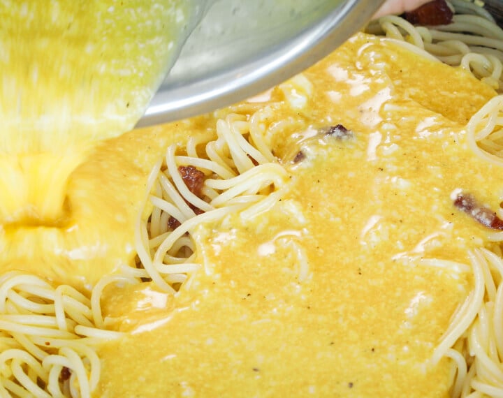 Step 5: Add the Egg Mixture for Cannabis Carbonara Pouring egg and cheese mixture over hot spaghetti in a pan, fifth step for making cannabis-infused carbonara sauce